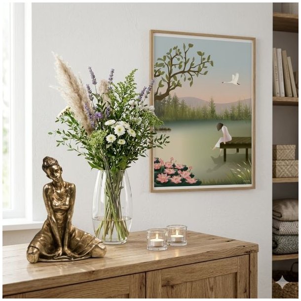 Et hyggeligt 1:1 milj�billede, der viser en curated tr�sk�nk. P� venstre side st�r en detaljeret bronze-skulptur af en siddende ballerina. Ved siden af hende st�r en elegant glaspokalvase fyldt med friske pampasgr�s og blomster. To sm� glasfyrfadslysholdere med t�ndte stearinlys fuldender opstillingen. Centreret p� v�ggen over sk�nken h�nger en indrammet Vissevasse-plakat med motivet af en kvinde p� en bro ved en s�, hvilket binder hele rummet sammen under bl�dt, naturligt dagslys.