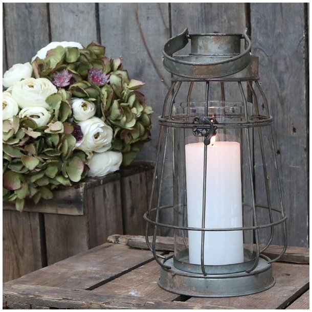 Et stemningsfuldt milj�billede i 1:1 format af en Factory lanterne i antique zink fra Chic Antique. Lanternen er t�ndt med et hvidt bloklys og st�r p� et rustikt tr�bord ved siden af en frodig buket blomster.