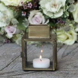 Et hyggeligt indend�rs milj�billede, hvor den lille messinglanterne st�r t�ndt med et fyrfadslys p� et rustikt tr�bord ved siden af en lille blomsterdekoration.