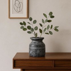 En m�rkegr� Metz cementkrukke med to eukalyptusgrene st�r p� en moderne sk�nk i lyst tr�. Ved siden af h�nger en enkel stregtegning i en tr�ramme p� en lys, neutral v�g.