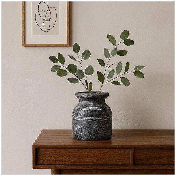 En m�rkegr� Metz cementkrukke med to eukalyptusgrene st�r p� en moderne sk�nk i lyst tr�. Ved siden af h�nger en enkel stregtegning i en tr�ramme p� en lys, neutral v�g.