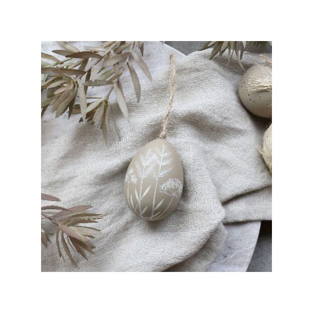 Dekorativt beige p�ske�g med hvidt bladm�nster h�ngende p� en for�rsgren i et lyst milj�.