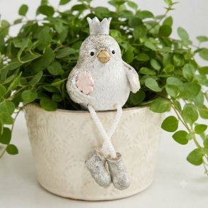 Lille beige og gr� dekorationsfugl med krone og h�ngeben, der sidder p� kanten af en hvid urtepotte med en gr�n plante.