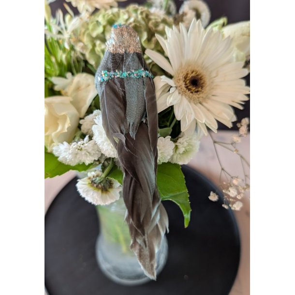Smuk turkis pyntefugl set oppefra, hvor den lange, m�rke fjerhale hviler elegant p� hvide blomster i en vase.