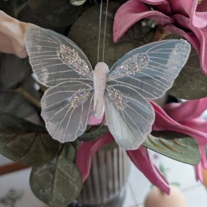 Gr�bl� pyntesommerfugl med glimmer sat fast p� m�rkegr�nne blade og lyser�de blomster i en vase.