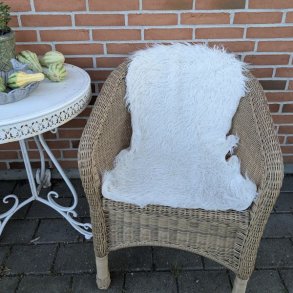 Et bl�dt hvidt kunstskind placeret over rygl�net p� en lys, naturfarvet fletstol, der viser skindets st�rrelse og dekorative effekt i indretningen.