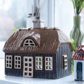 Stort bl�t keramikhus med brunt str�tag fra Det Gamle Apotek placeret i en lys vindueskarm ved siden af en vase med lavendler