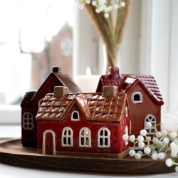 Tre r�de keramikhuse fra Det Gamle Apotek samlet som juledekoration p� en m�rk tr�bakke i en vindueskarm sammen med hvide brudesl�r-blomster