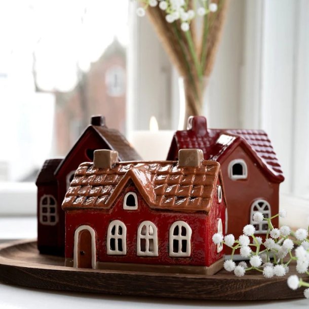 Tre r�de keramikhuse fra Det Gamle Apotek samlet som juledekoration p� en m�rk tr�bakke i en vindueskarm sammen med hvide brudesl�r-blomster