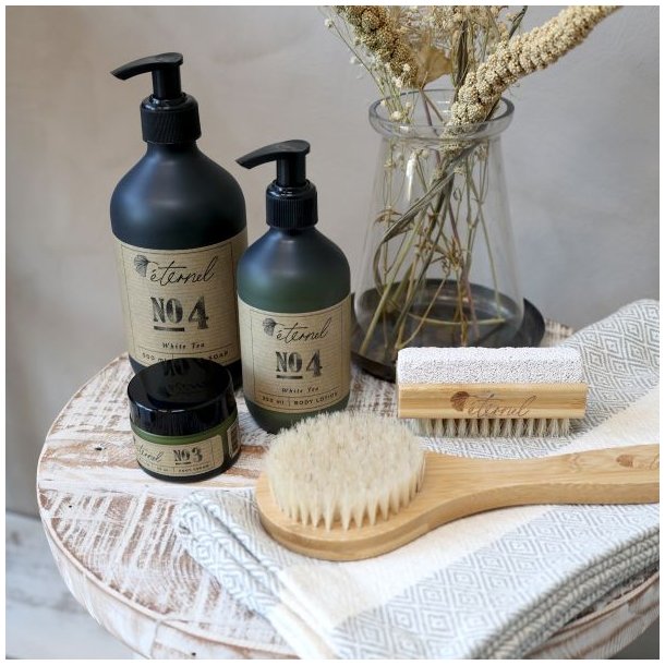 Milj�billede af Eternel plejeprodukter p� en tr�bakke, herunder negleb�rsten og h�rb�rsten, der viser produkternes naturlige sammenh�ng.