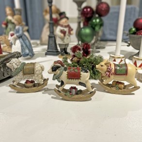 tre s�de julefigurer af et f�r, en ko og en gris udformet som gyngeheste opstillet p� en hvid overflade