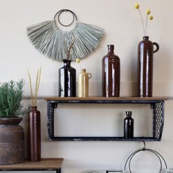 En dekorativ v�gopstilling med forskellige brune keramikvaser og flasker p� en sort metalhylde. Den store flaske med hank st�r til h�jre med tre gule blomster i.