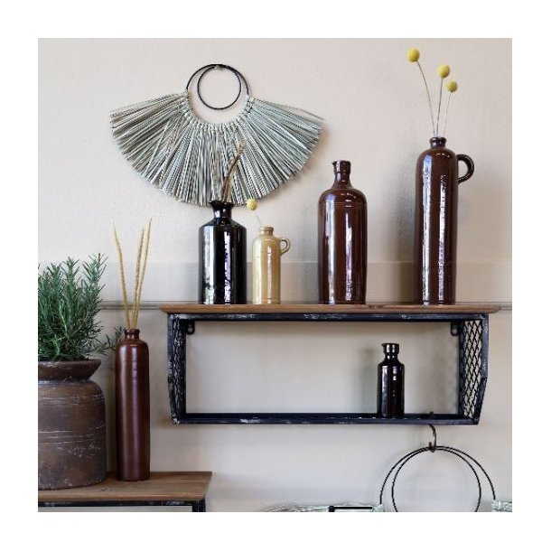 En stemningsfuld v�gdekoration med flere brune keramikflasker i forskellige st�rrelser placeret p� r� tr�hylder. Den mocca-brune flaske med h�ldetud ses her i en smuk kombination med naturmaterialer og gr�nne planter.