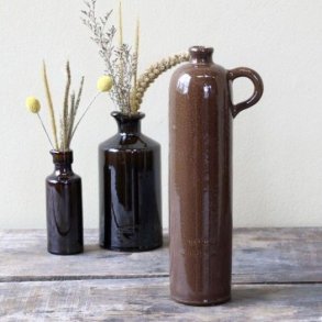 Den brune keramikflaske st�r p� et rustikt tr�bord ved siden af to mindre brune flasker med t�rrede blomster og gule trommestikker