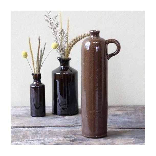 Den brune keramikflaske st�r p� et rustikt tr�bord ved siden af to mindre brune flasker med t�rrede blomster og gule trommestikker