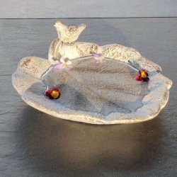 Vandt�t bladformet fuglebad i creme-hvid og guld patina med en lille fugl p� kanten og vand med sm� blomster.