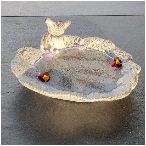 Vandt�t bladformet fuglebad i creme-hvid og guld patina med en lille fugl p� kanten og vand med sm� blomster.