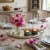Hvid spejlbakke p� et d�kket spisebord med to glasfyrfadsholdere med patineret gr�n bund og en lille vase med rosa blomster.