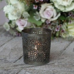 T�ndt fyrfadsstage i antique messing med hulm�nster, opstillet i et hyggeligt milj� med blomster i baggrunden.