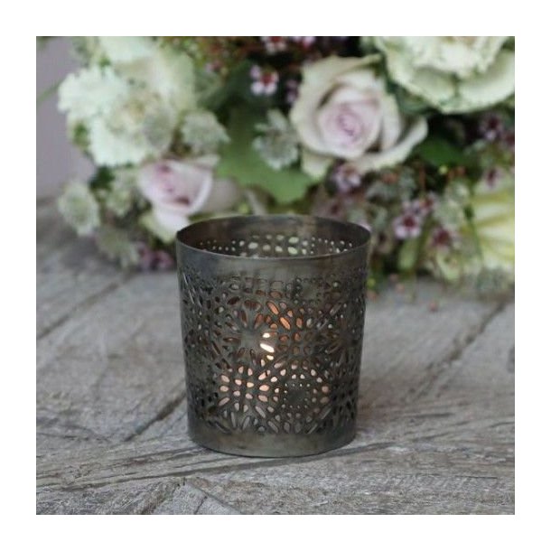 T�ndt fyrfadsstage i antique messing med hulm�nster, opstillet i et hyggeligt milj� med blomster i baggrunden.