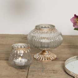 Et n�rbillede i 1:1 format af den t�ndte fyrfadsstage i klart glas p� et rustikt tr�bord. Ved siden af ses den tilh�rende store glasbonbonniere p� guld fod og en spejlbakke, hvilket skaber en hyggelig og sammenh�ngende dekoration.