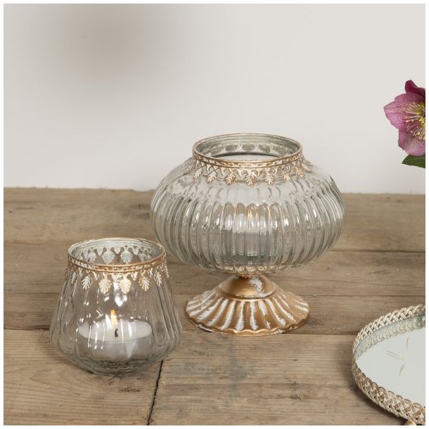 Et n�rbillede i 1:1 format af den t�ndte fyrfadsstage i klart glas p� et rustikt tr�bord. Ved siden af ses den tilh�rende store glasbonbonniere p� guld fod og en spejlbakke, hvilket skaber en hyggelig og sammenh�ngende dekoration.