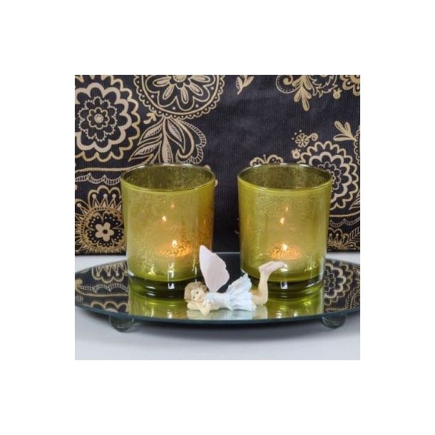 Et stemningsfuldt milj�billede i 1:1 format, der viser to t�ndte fyrfadsstager i klart glas med det specifikke gr�nne bladm�nster, baseret p� image_86.png. De st�r p� en rund spejlbakke ved siden af en lille dekorativ alf-figur, mod en baggrund med et matchende sort og guld m�nstret tapet.