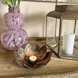 Fyrfadsstage formet som en lotusblomst i antik brun jern med t�ndt lys p� et tr�bord ved siden af en vase med blomster og lanterne.