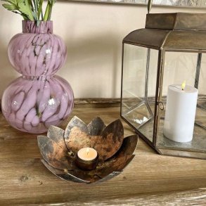 Fyrfadsstage formet som en lotusblomst i antik brun jern med t�ndt lys p� et tr�bord ved siden af en vase med blomster og lanterne.