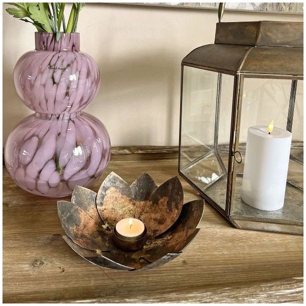 Fyrfadsstage formet som en lotusblomst i antik brun jern med t�ndt lys p� et tr�bord ved siden af en vase med blomster og lanterne.