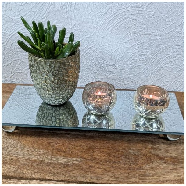 To m�nstrede fyrfadsstager i antique s�lv med t�ndte lys og en gr�n potteplante arrangeret p� et rektangul�rt spejlplateau.