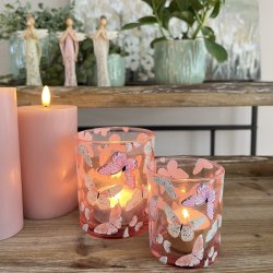 o t�ndte sommerfugle-fyrfadsstager i rosa og lysegr�n glas p� et bord med planter.