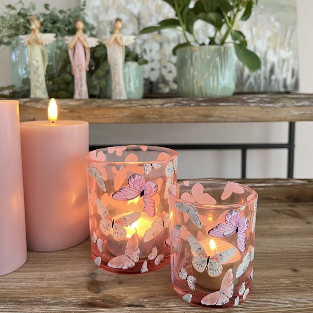 o t�ndte sommerfugle-fyrfadsstager i rosa og lysegr�n glas p� et bord med planter.