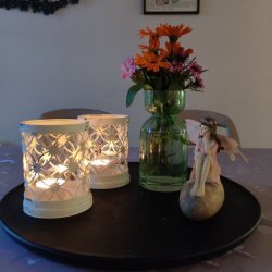 Gr�n glasvase med en buket orange og lilla blomster placeret p� et sort dekorationsfad sammen med r�hvide fyrfadsstager.