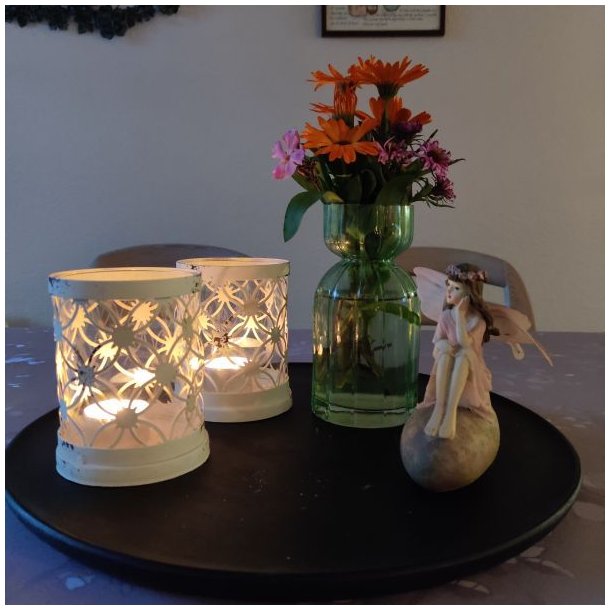 Gr�n glasvase med en buket orange og lilla blomster placeret p� et sort dekorationsfad sammen med r�hvide fyrfadsstager.