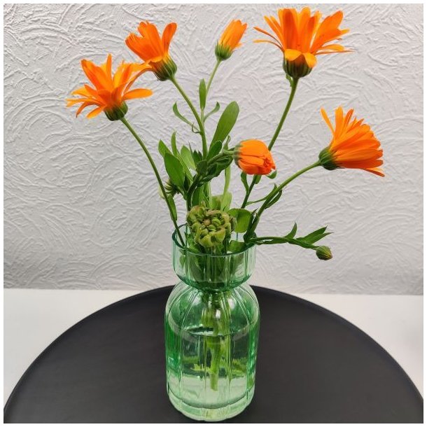 Gr�n rillet glasvase i to niveauer fyldt med friske orange morgenfruer st�ende p� et sort fat.