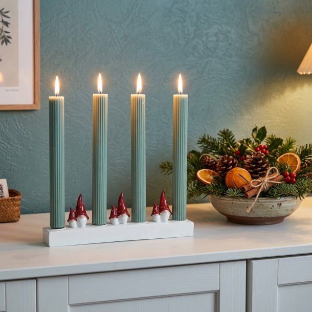 Stemningsfuldt firkantet milj�billede af Harvesttime adventsstagen med t�ndte gr�nne lys placeret p� en hvid sk�nk ved siden af en juledekoration.