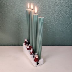 Stemningsfuldt produktbillede set fra vinkel af Harvesttime adventsstagen med t�ndte gr�nne lys p� en bordflade foran en gr�n v�g.