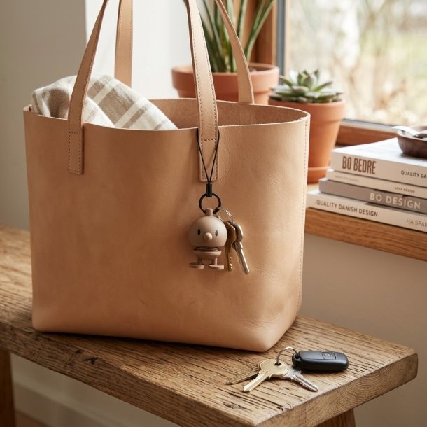 Latte-farvet Hoptimist Bag Charm taskevedh�ng i silikone placeret p� en l�dertaske.
