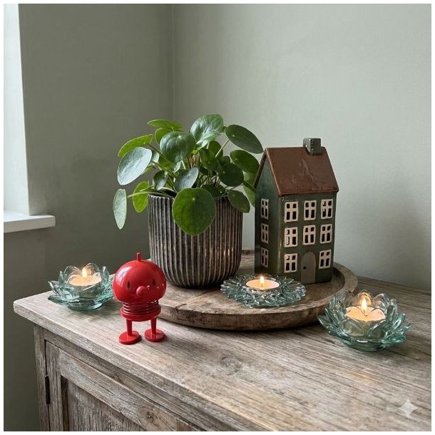 En samling af fire unikke gr�nlige glasfyrfadsstager, en m�rk ribbed keramikurtepotte med en frodig Pilea-plante, og et m�rkegr�nt keramikhus arrangeret p� en rustik tr�overflade, med en lille r�d Hoptimist figur i forgrunden, i et kvadratisk milj�billede.