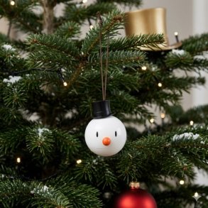 Et firkantet 1:1 milj�billede af et Snowman ornament fra Hoptimist, formet som en hvid snemand med sort h�j hat, gulerodsn�se og en diameter p� 6 cm, der h�nger i en snor p� gr�nne grangrene p� et juletr� pyntet med varme julelys og en r�d julekugle.