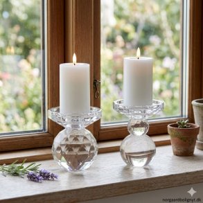 Hvide LED-bloklys med en diameter p� 7,5 cm placeret i smukke krystallysestager i en vindueskarm. Lysene har en realistisk flammeeffekt, og i baggrunden anes et gr�nt havemilj� gennem vinduet