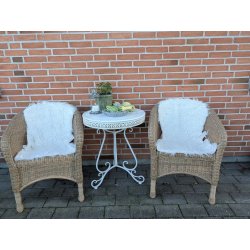 t hvidt imiteret lammeskind lagt over s�det p� en naturfarvet flettet havestole ved havebord for at skabe en hyggelig og bl�d siddeplads.