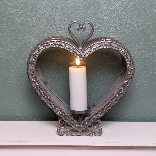 Hvidt LED bloklys med t�ndt flamme placeret i en vintage hjerteformet metal lanterne p� en hvid hylde.
