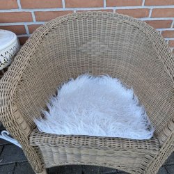 En naturfarvet flettet havestol stylet med et hvidt firkantet imiteret lammeskind som bl�d s�dehynde.