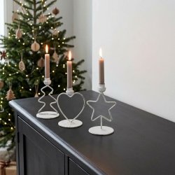 Stemningsfuldt firkantet milj�billede af de tre jule lysestager i antique hvid metal med t�ndte gr� stagelys, st�ende p� en m�rk sk�nk foran et oplyst juletr�.