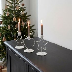 Stemningsfuldt firkantet milj�billede af de tre jule lysestager i antique hvid metal med t�ndte gr� stagelys, st�ende p� en m�rk sk�nk foran et oplyst juletr�.