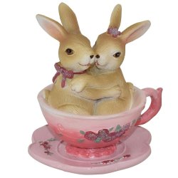 Dekorationsfigur af to naturfarvede kaniner der krammer i en lyser�d kop med blomstermotiv.