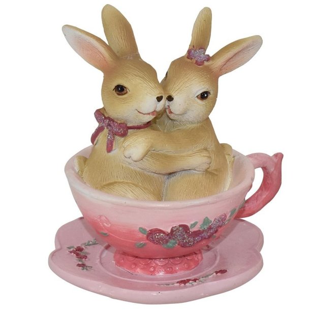 Dekorationsfigur af to naturfarvede kaniner der krammer i en lyser�d kop med blomstermotiv.