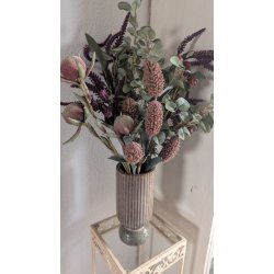 Den lille brune keramikvase dekoreret med en smuk buket af lyser�de liljer, t�rrede fr�stande og en h�ngende gr�n perler-p�-en-snor plante mod en hvid baggrund.